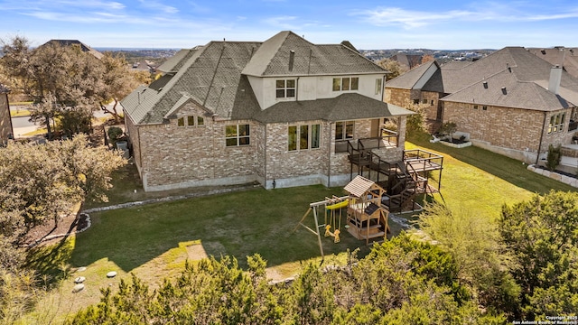 rear view of property with a yard, a playground, and a deck