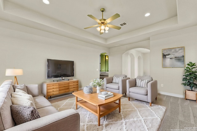 carpeted living room with ceiling fan and a tray ceiling