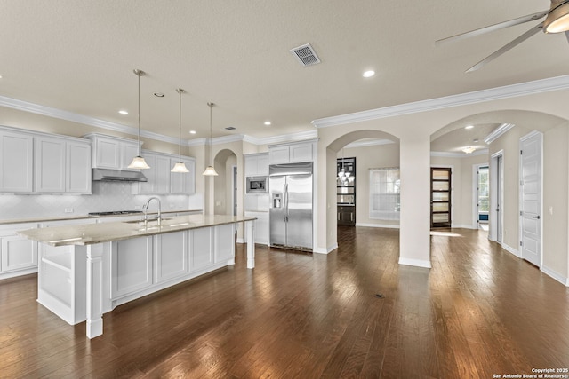 kitchen featuring white cabinets, built in appliances, decorative backsplash, an island with sink, and decorative light fixtures