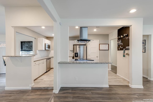 kitchen featuring white cabinets, a kitchen island, light stone countertops, appliances with stainless steel finishes, and island range hood