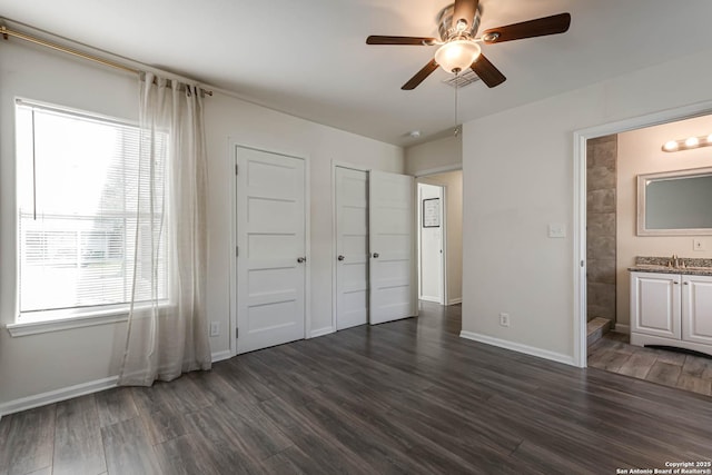 unfurnished bedroom with ceiling fan, two closets, dark wood-type flooring, and ensuite bath