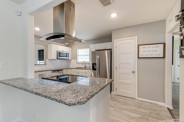 kitchen with kitchen peninsula, light stone countertops, island exhaust hood, stainless steel appliances, and white cabinetry