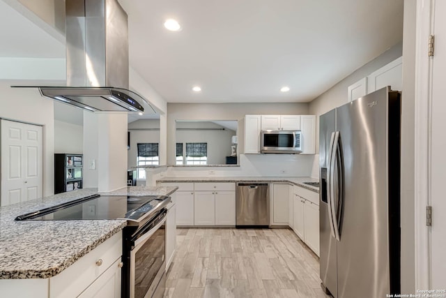 kitchen featuring white cabinetry, light stone counters, island exhaust hood, kitchen peninsula, and appliances with stainless steel finishes