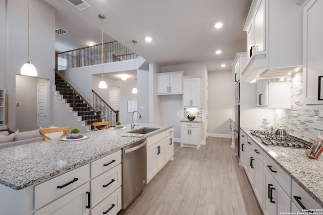 kitchen with light stone countertops, stainless steel appliances, sink, white cabinets, and hanging light fixtures