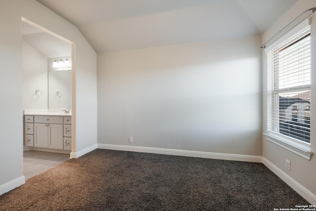 interior space with ensuite bath, sink, light colored carpet, and vaulted ceiling