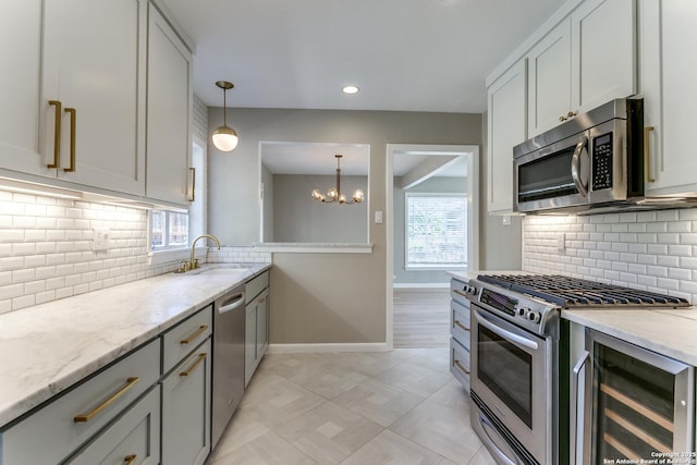 kitchen with sink, light stone counters, a chandelier, decorative light fixtures, and appliances with stainless steel finishes