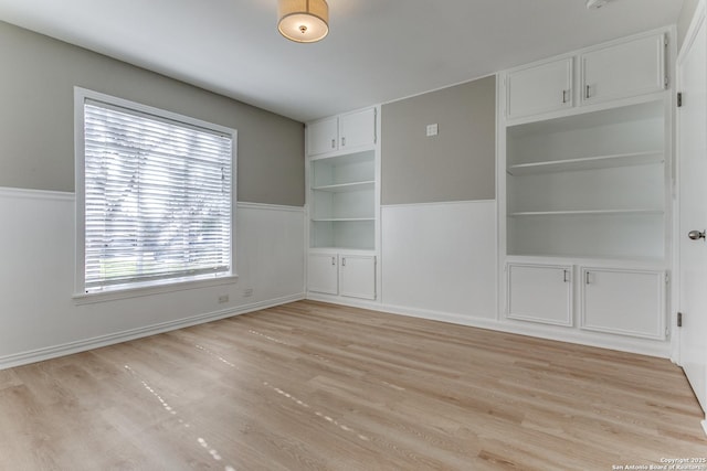 unfurnished room featuring built in shelves and light wood-type flooring