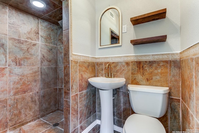 bathroom with sink, tiled shower, toilet, and tile walls