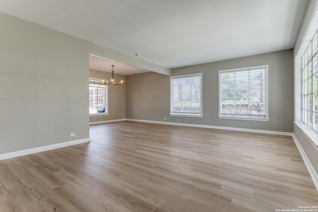 unfurnished room featuring a healthy amount of sunlight, light wood-type flooring, and a notable chandelier