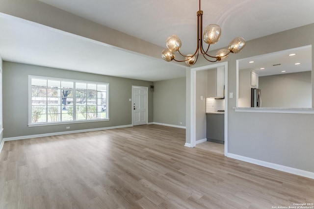 unfurnished living room with a notable chandelier and light hardwood / wood-style floors