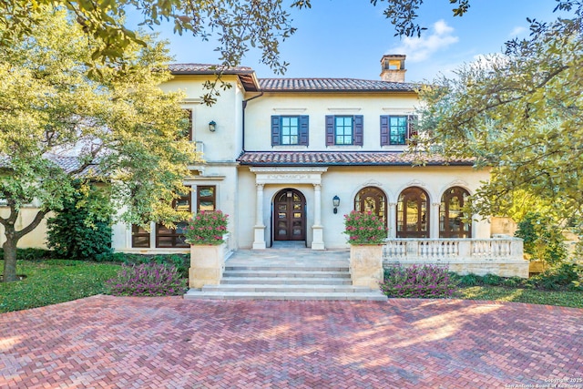 mediterranean / spanish home featuring a chimney, a tiled roof, covered porch, french doors, and stucco siding