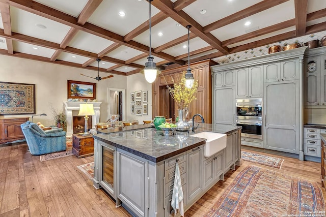 kitchen featuring light wood finished floors, coffered ceiling, a fireplace, and a sink