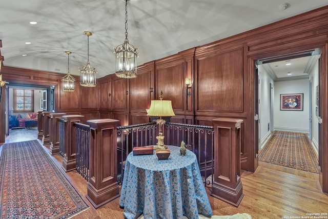 bar featuring light wood-style flooring, vaulted ceiling, crown molding, pendant lighting, and a decorative wall