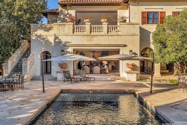 back of house featuring a tile roof, a patio area, a balcony, and stucco siding