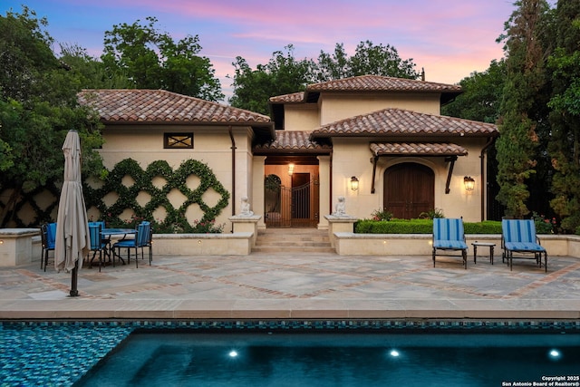 200 Geneseo Rd, Terrell Hills, TX 78209 - back of house at dusk with a tile roof, a patio area, an outdoor pool, and stucco siding