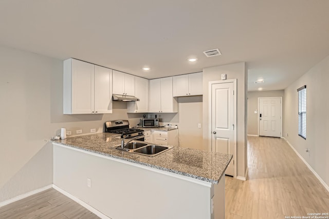 kitchen featuring kitchen peninsula, appliances with stainless steel finishes, white cabinetry, and light stone counters