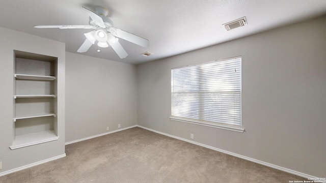 spare room with light colored carpet, built in features, and ceiling fan