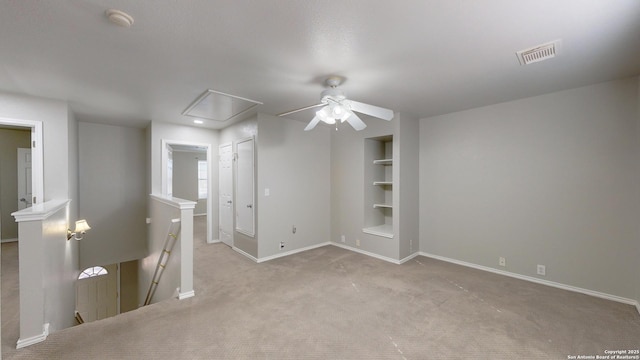 empty room featuring light carpet, built in shelves, and ceiling fan