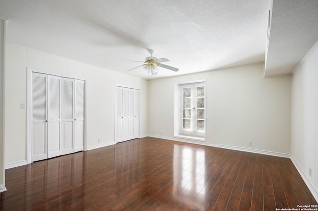 unfurnished bedroom with ceiling fan, dark hardwood / wood-style floors, a textured ceiling, and multiple closets