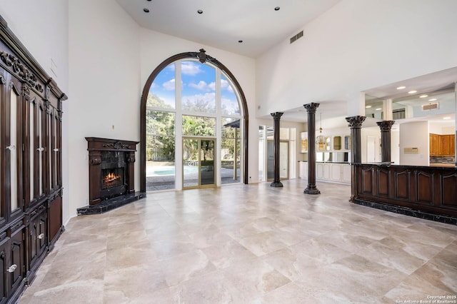 unfurnished living room featuring a towering ceiling, a fireplace, and ornate columns