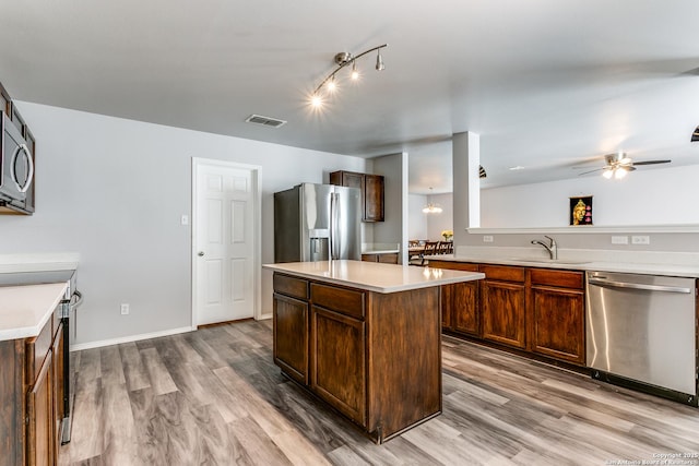 kitchen with light wood-type flooring, stainless steel appliances, ceiling fan, sink, and a center island