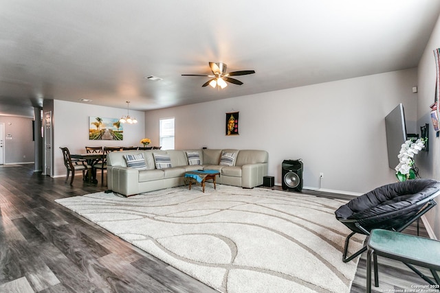 living room featuring ceiling fan with notable chandelier and dark wood-type flooring