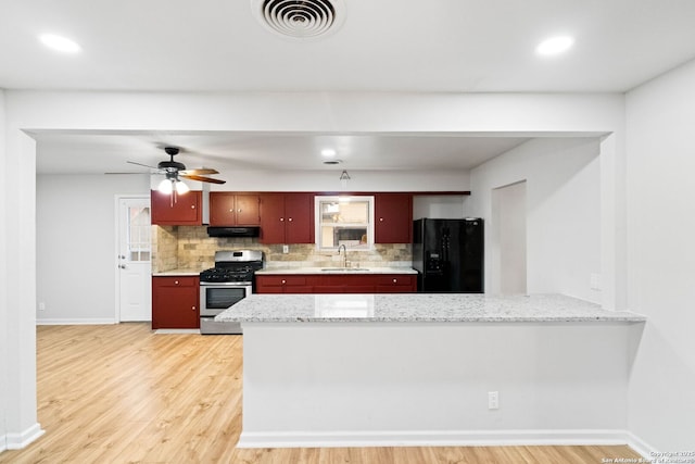 kitchen featuring black refrigerator, sink, tasteful backsplash, kitchen peninsula, and stainless steel range with gas stovetop