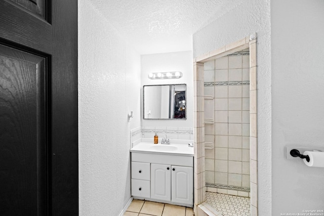 bathroom with tile patterned floors, vanity, a tile shower, and a textured ceiling