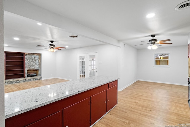 kitchen with ceiling fan, a stone fireplace, light wood-type flooring, and french doors