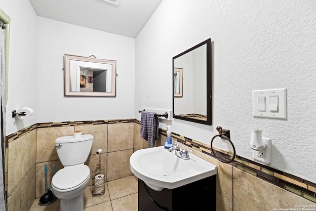 bathroom with toilet, vanity, tile patterned floors, and tile walls