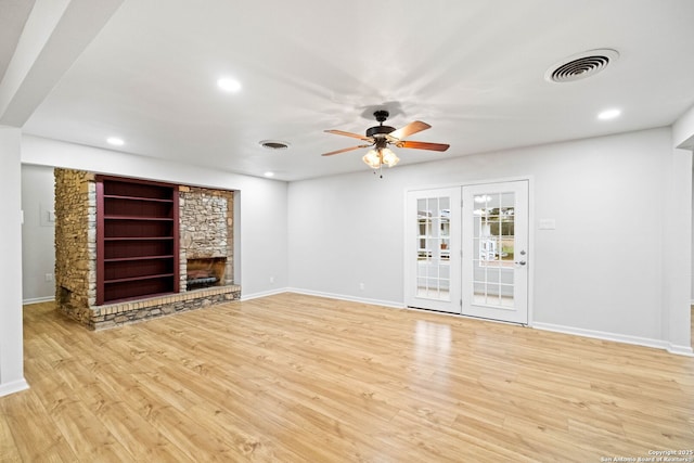 unfurnished living room featuring ceiling fan, a fireplace, french doors, and light wood-type flooring