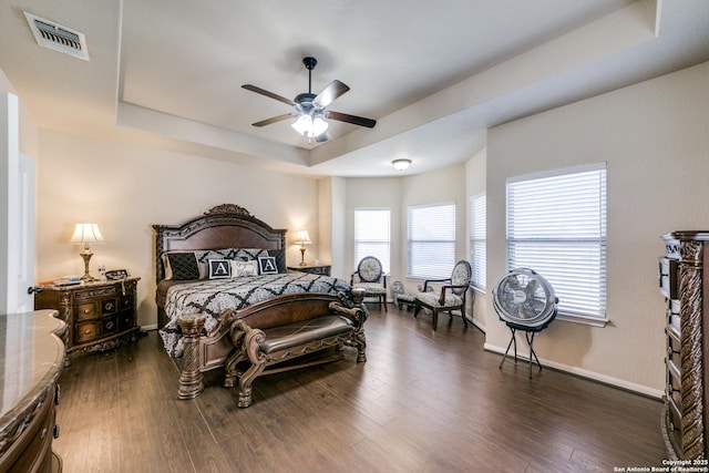 bedroom featuring ceiling fan, a tray ceiling, and dark wood-type flooring