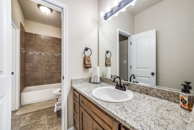 bathroom with a textured ceiling, vanity, and tiled shower / bath