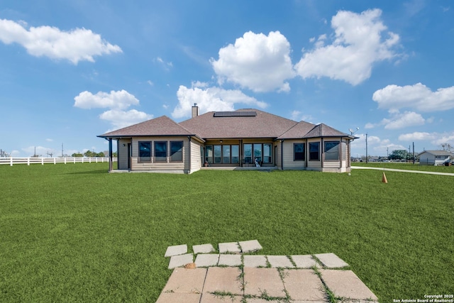 rear view of house featuring a yard and solar panels