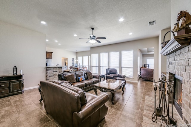 living room featuring a brick fireplace, a textured ceiling, and ceiling fan