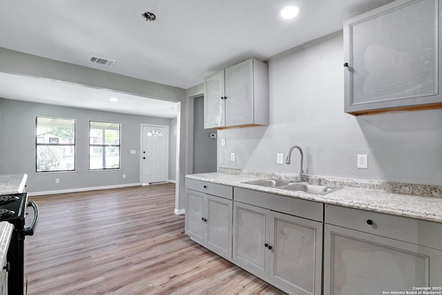 kitchen featuring stainless steel stove, light hardwood / wood-style floors, gray cabinetry, and sink