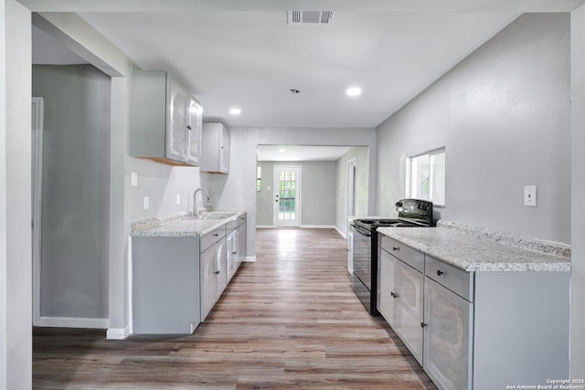 kitchen with light stone countertops, black range with electric cooktop, sink, light hardwood / wood-style floors, and white cabinetry