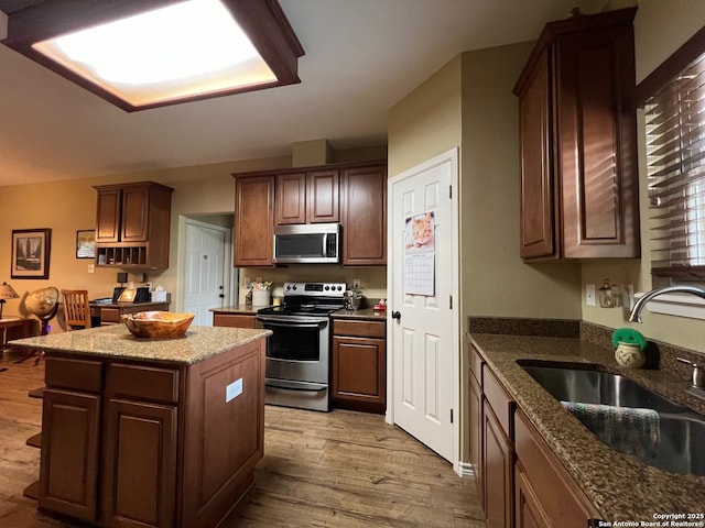 kitchen featuring a center island, dark stone counters, sink, light hardwood / wood-style flooring, and appliances with stainless steel finishes