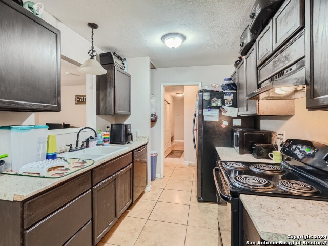 kitchen featuring sink, a textured ceiling, decorative light fixtures, light tile patterned flooring, and black appliances