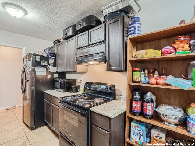 kitchen with a textured ceiling, black range with electric cooktop, fridge, light tile patterned flooring, and dark brown cabinetry