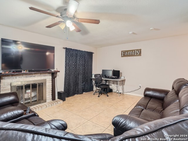 living room featuring ceiling fan, light tile patterned floors, and a brick fireplace