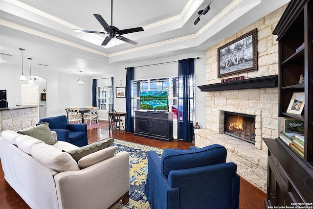 living room with a tray ceiling, ceiling fan, a fireplace, and dark hardwood / wood-style floors