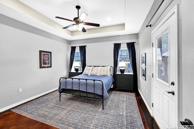 bedroom featuring a textured ceiling, dark hardwood / wood-style flooring, a raised ceiling, and ceiling fan