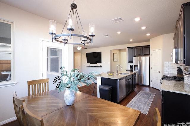 kitchen with a center island with sink, tasteful backsplash, decorative light fixtures, light stone counters, and stainless steel appliances