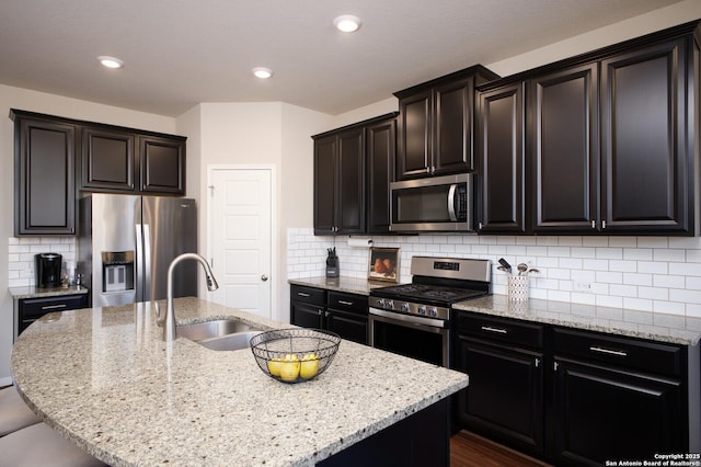 kitchen featuring decorative backsplash, stainless steel appliances, a center island with sink, and sink