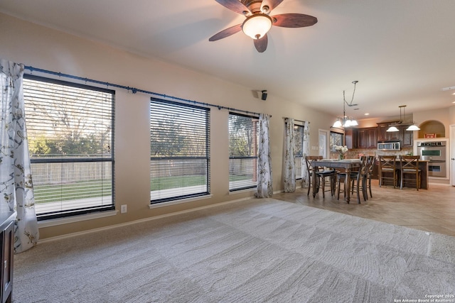 unfurnished dining area with light carpet, ceiling fan with notable chandelier, and plenty of natural light