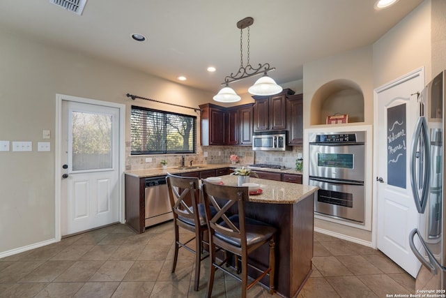 kitchen with dark brown cabinets, stainless steel appliances, sink, decorative light fixtures, and a kitchen island