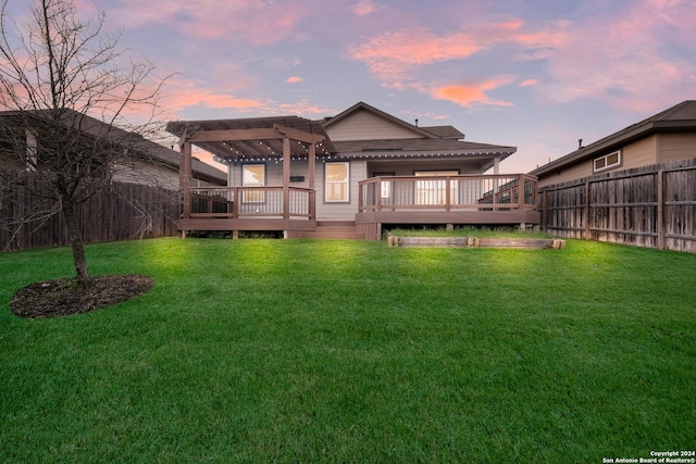 back house at dusk featuring a pergola, a wooden deck, and a yard