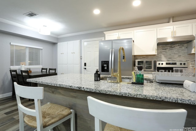 kitchen featuring a breakfast bar, white cabinets, light stone countertops, ornamental molding, and stainless steel appliances