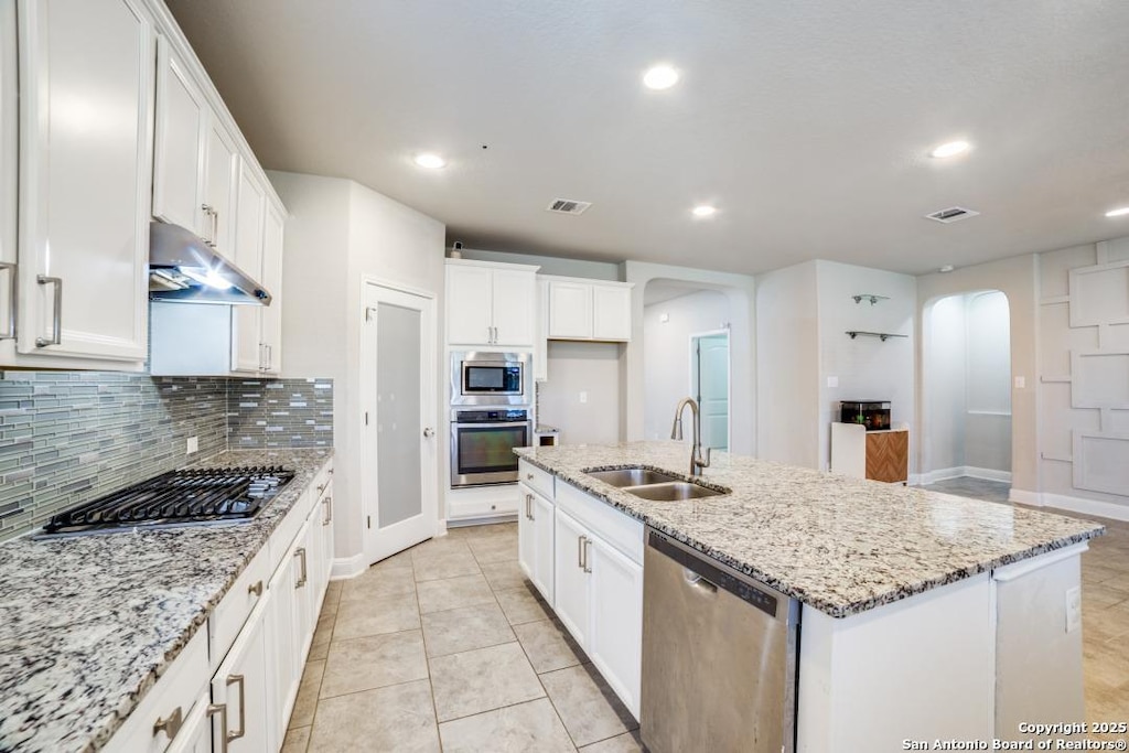 kitchen featuring white cabinets, sink, an island with sink, light stone counters, and stainless steel appliances